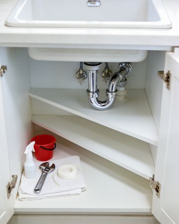 A newly fitted chrome drain trap under a kitchen sink with a wrench and thread tape