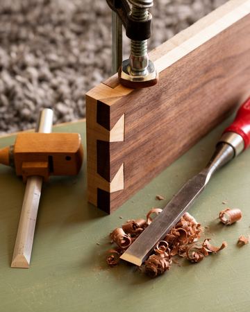 A hand-cut dovetail joint in walnut clamped on a bench beside a chisel